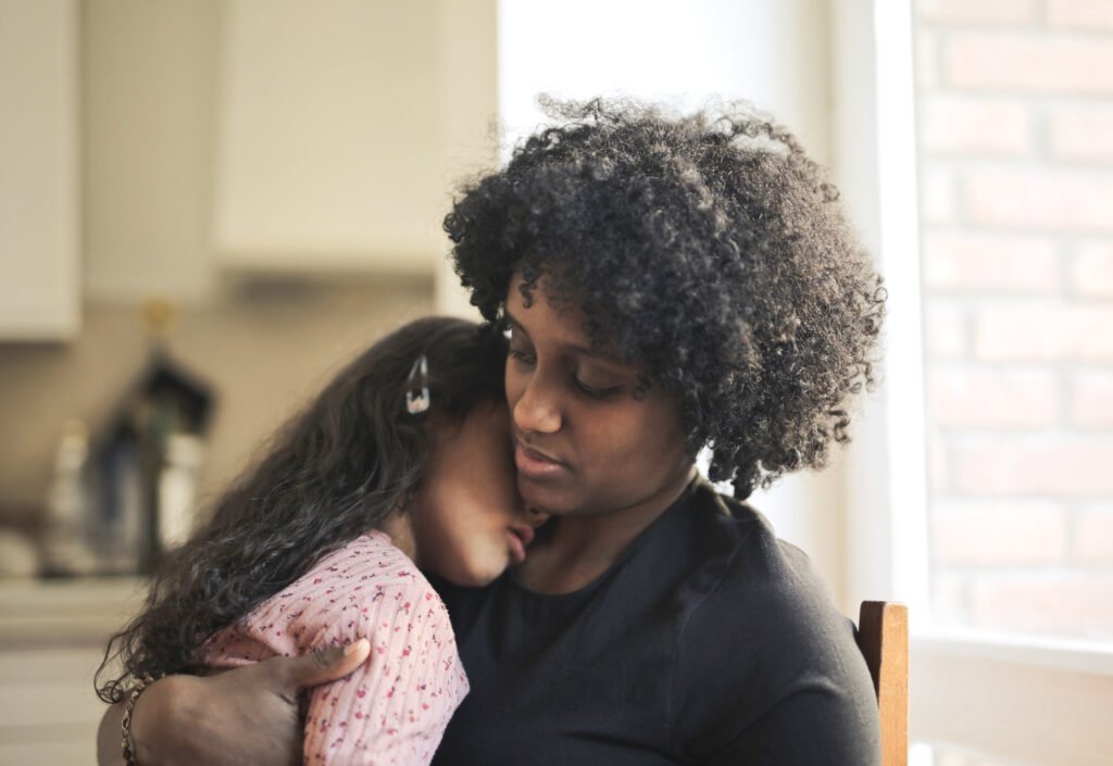 Shallow focus of a tired multi-racial kid hugging her black mother at home